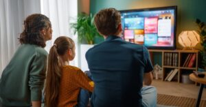 Sala decorada moderna exibindo um elegante painel de tv planejado para sala pequena em madeira clara com iluminação LED e uma TV HQ 60 Polegadas instalada.